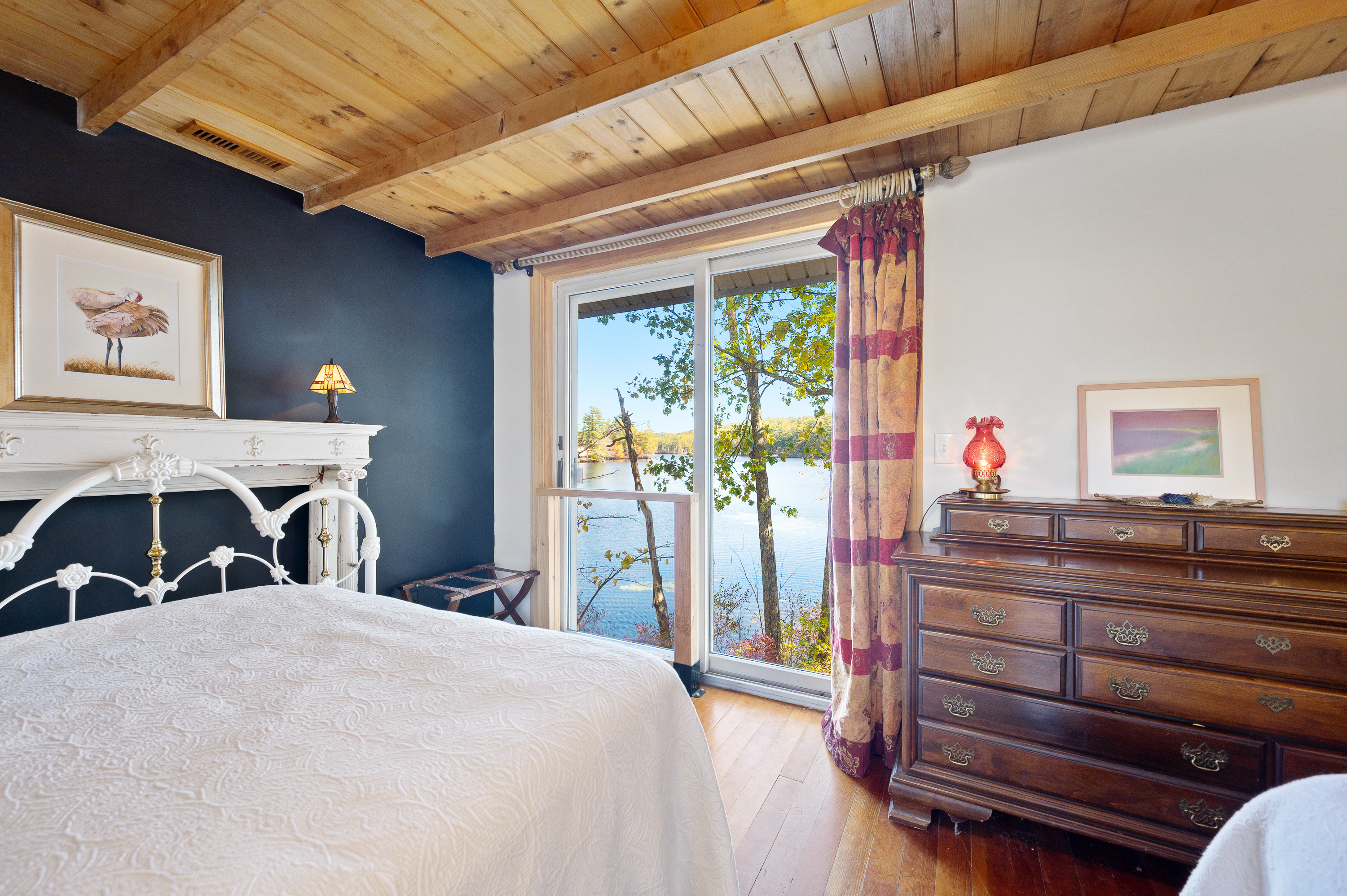 Cozy bedroom with wood ceiling and large window overlooking water.