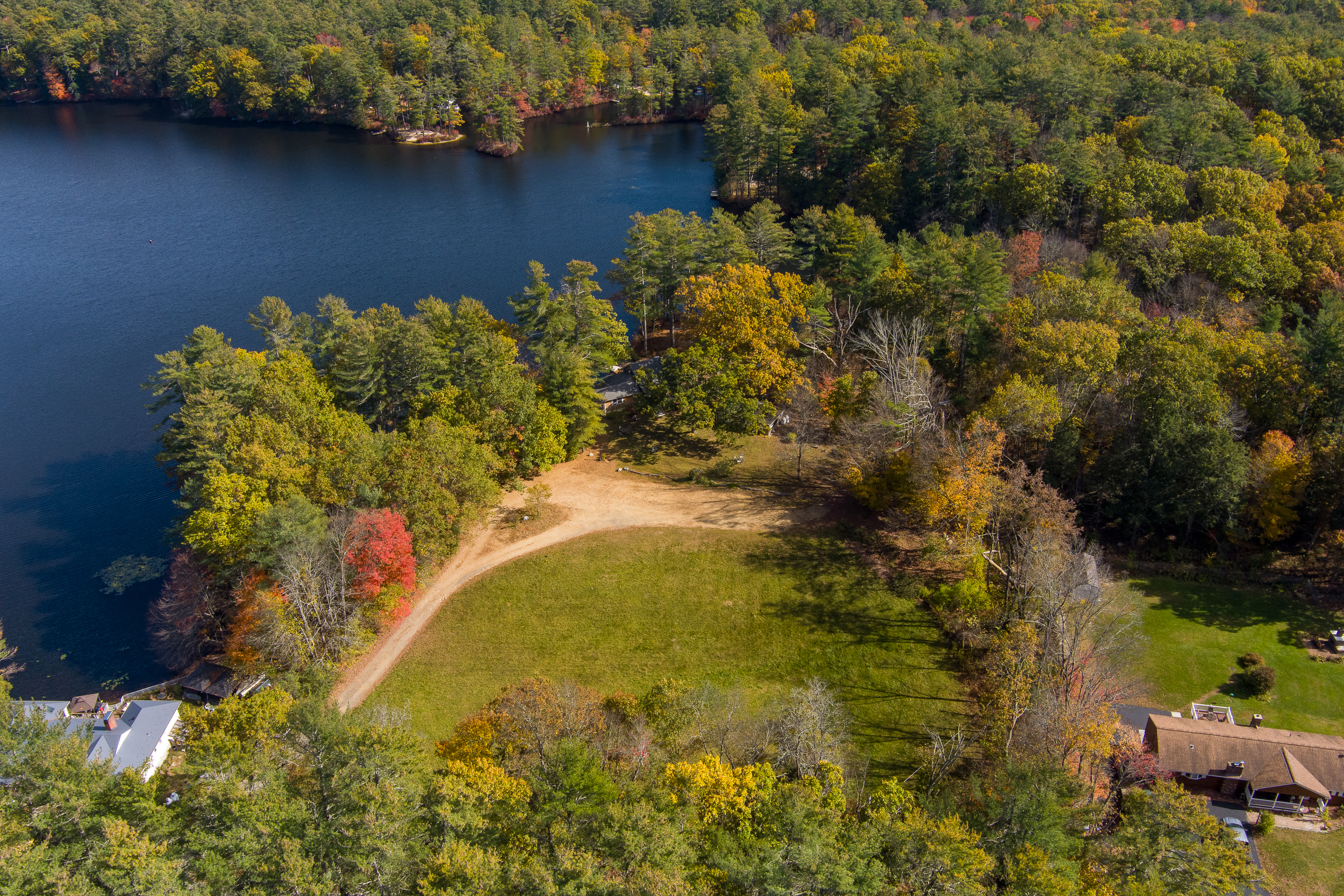 Aerial view of a winding dirt path near a lake surrounded by autumn trees.
