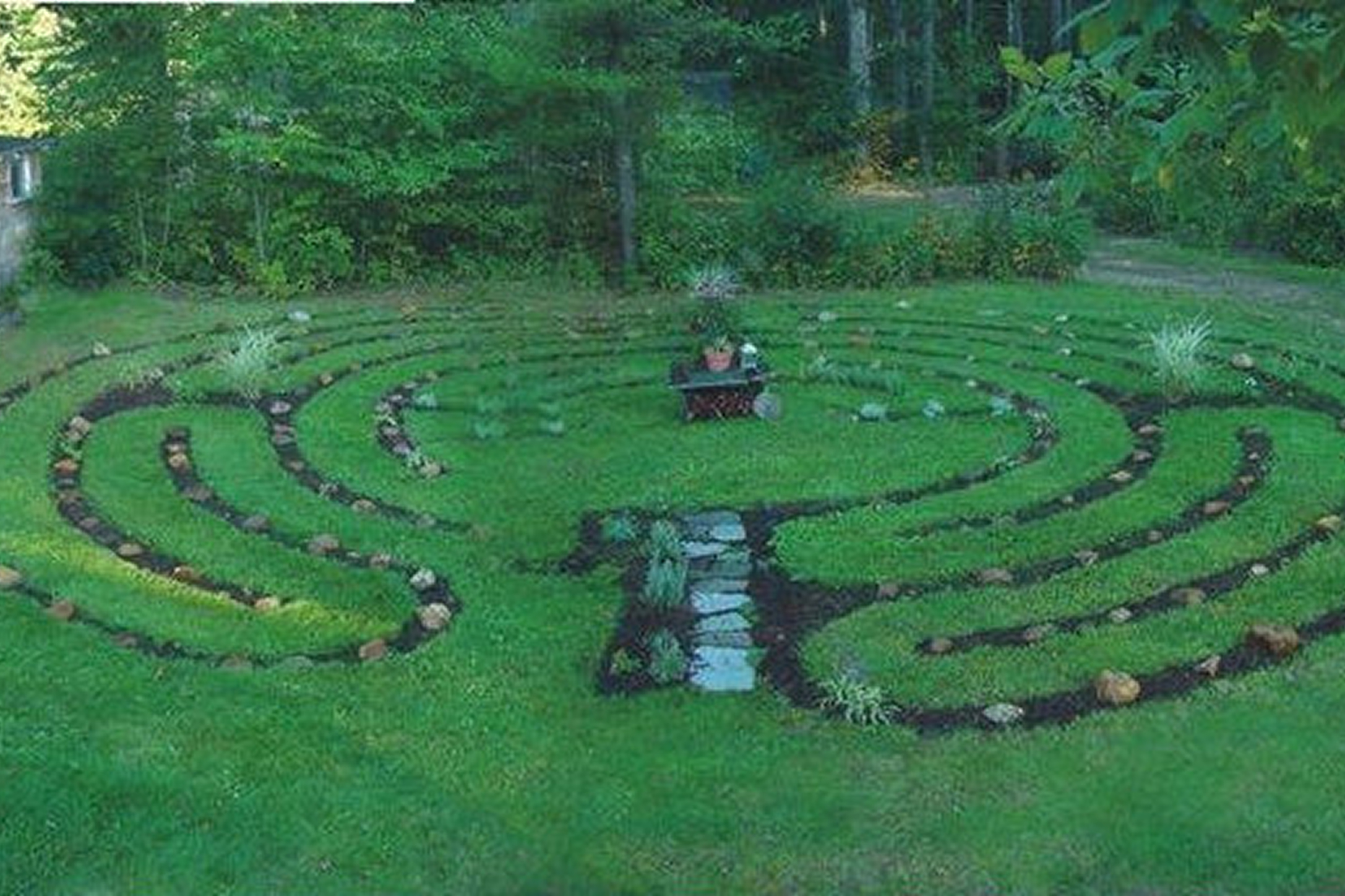 A peaceful garden labyrinth with green grass and stone pathways.