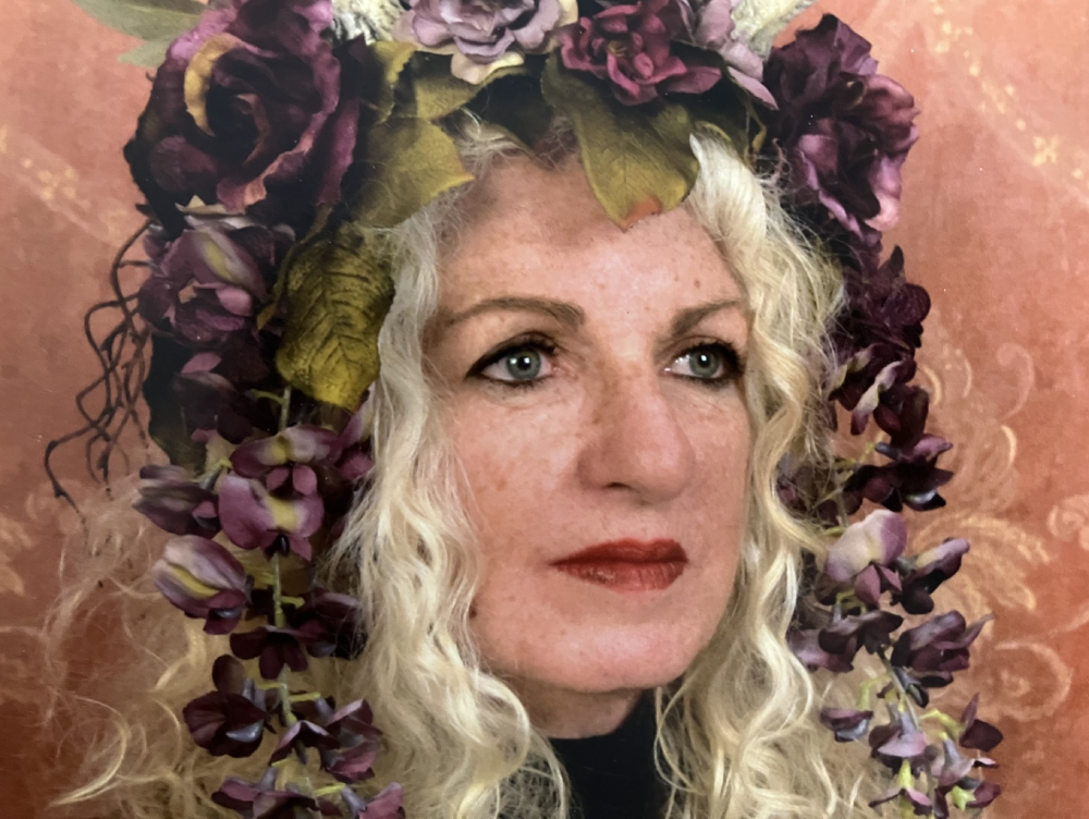 Woman with curly blonde hair adorned with purple flowers.