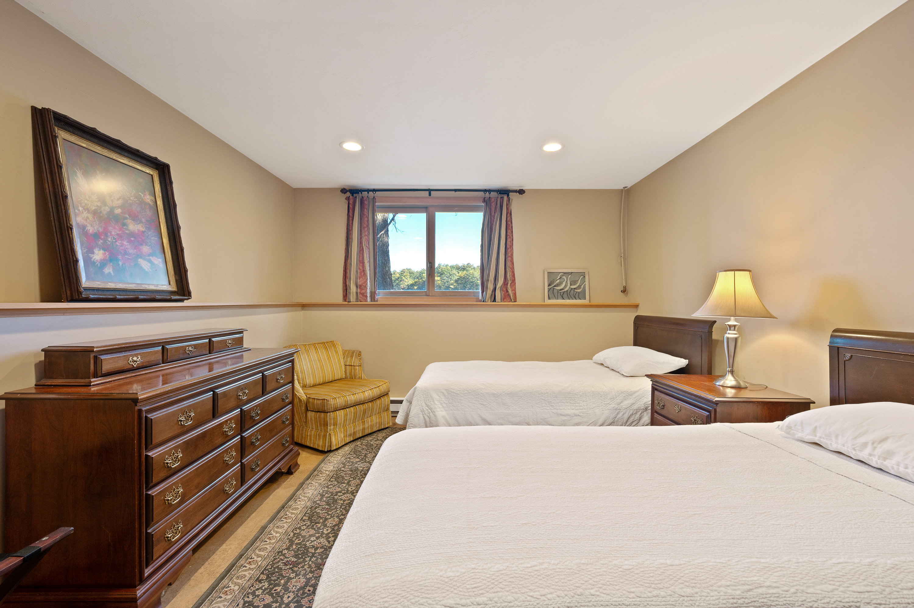 Cozy bedroom with twin beds, a wooden dresser, and a window with blue curtains.